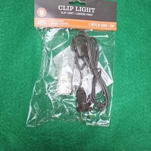 May include: A package containing a black clip light with a 5W bulb. The package is labeled "Clip Light" and "1 Bulb 120V/5W".