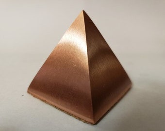 May include: A small, copper-colored pyramid with a smooth, brushed finish.