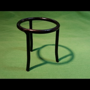May include: A black metal ring stand with three legs. The stand is on a green surface.