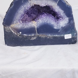 May include: A large amethyst geode with a purple and white interior. The geode is half-cut and has a dark grey exterior. The geode is labelled with the numbers "460" and "1057".