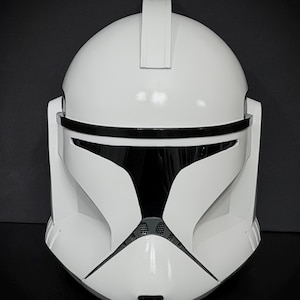 May include: A white and black helmet with a glossy finish. The helmet has a rounded top with a rectangular ridge and a black visor. The design includes a detailed front with ventilation and a chin strap.