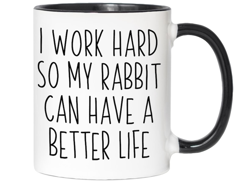 May include: White ceramic mug with a black interior and handle. The mug features the text "I WORK HARD SO MY RABBIT CAN HAVE A BETTER LIFE" in black, handwritten-style lettering. A fun gift for rabbit owners.