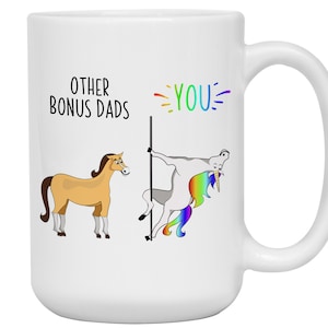 May include: White ceramic mug with a humorous design. The mug features the text "OTHER BONUS DADS" and "YOU" in rainbow colors, along with cartoon illustrations of a horse and a unicorn. The unicorn is pole dancing.