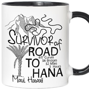 K&ouml;nnte beinhalten: Wei&szlig;er Keramikbecher mit schwarzem Griff und Rand, mit dem Text "Survivor of Road to Hana" und einer Illustration von Berg und Palme. Enth&auml;lt den Text "Maui, Hawaii".