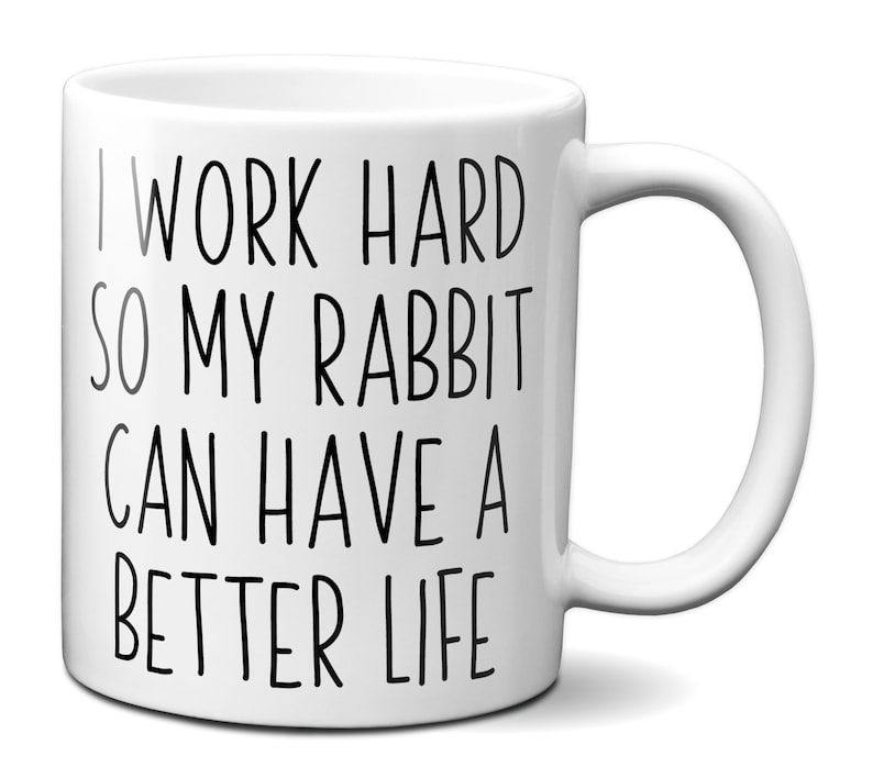 May include: White ceramic mug with a curved handle. The mug features black text that reads: "I WORK HARD SO MY RABBIT CAN HAVE A BETTER LIFE."