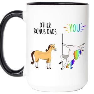 May include: White ceramic mug with a black handle and rim. The mug features the text "OTHER BONUS DADS" and the word "YOU" in rainbow colors. Illustrations of a horse and a unicorn are also on the mug.