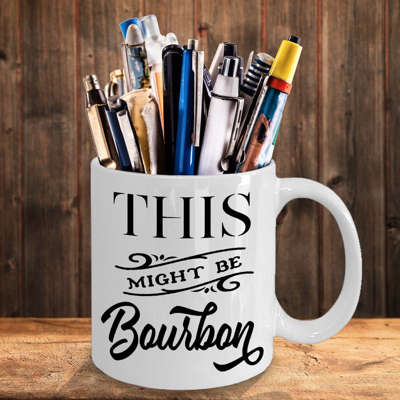Puede incluir: Taza de cer&aacute;mica blanca con el texto "THIS MIGHT BE Bourbon" en escritura negra. La taza est&aacute; llena de bol&iacute;grafos y rotuladores de varios colores y dise&ntilde;os. La taza tiene un asa grande y est&aacute; sobre una superficie de madera.