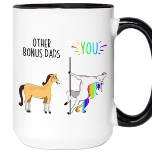May include: White ceramic mug with a black handle and rim. The mug features a humorous design with the text "OTHER BONUS DADS" and "YOU" in rainbow colors. Illustrations of a horse and a unicorn are also present.
