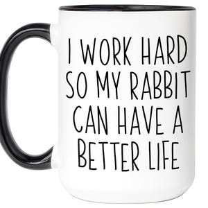 May include: White ceramic mug with a black handle and rim. The mug features the text "I WORK HARD SO MY RABBIT CAN HAVE A BETTER LIFE" in black, bold letters. A fun gift for rabbit owners.