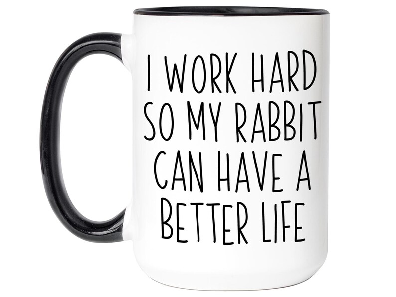 May include: White ceramic mug with a black handle and rim. The mug features the text "I WORK HARD SO MY RABBIT CAN HAVE A BETTER LIFE" in black, bold letters. A fun gift for rabbit owners.