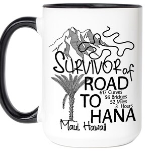 K&ouml;nnte beinhalten: Wei&szlig;er Keramikbecher mit schwarzem Henkel und Rand. Der Becher hat ein schwarz-wei&szlig;es Design mit dem Text "Survivor of Road to Hana" und enth&auml;lt eine Bergillustration, eine Palme und Statistiken &uuml;ber die Stra&szlig;e.