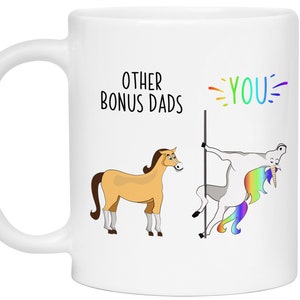 May include: White ceramic mug with a humorous design. The mug features the text "OTHER BONUS DADS" and "YOU" in colorful lettering. The design includes cartoon horses and a unicorn.