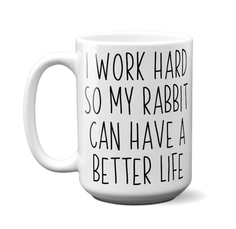May include: White ceramic mug with a curved handle. The mug features black text that reads, "I WORK HARD SO MY RABBIT CAN HAVE A BETTER LIFE."