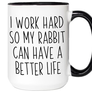 May include: White ceramic mug with a black handle and rim. The mug features the text "I WORK HARD SO MY RABBIT CAN HAVE A BETTER LIFE" in black, centered on the front. A humorous and heartwarming gift for rabbit owners.