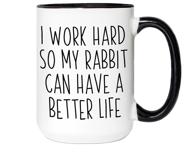 May include: White ceramic mug with a black handle and rim. The mug features the text "I WORK HARD SO MY RABBIT CAN HAVE A BETTER LIFE" in black, centered on the front. A humorous and heartwarming gift for rabbit owners.