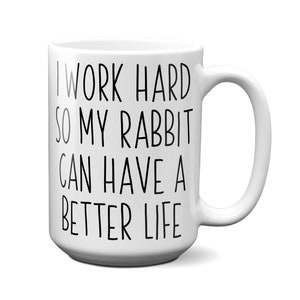 May include: White ceramic mug with a curved handle. The mug features black text that reads, "I WORK HARD SO MY RABBIT CAN HAVE A BETTER LIFE."