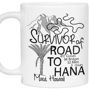 K&ouml;nnte beinhalten: Wei&szlig;e Keramik-Tasse mit schwarzem Grafikdesign. Das Design umfasst einen Berg, eine Palme und den Text "Survivor of Road to Hana" mit Angaben zu Kilometerstand und Zeit. "Maui, Hawaii" ist ebenfalls aufgedruckt.