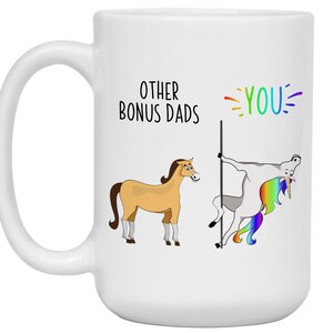 May include: White ceramic mug with a humorous design. The mug features two cartoon horses, one a standard horse and the other a unicorn, with the text "OTHER BONUS DADS" and "YOU" in colorful lettering. A fun gift idea.