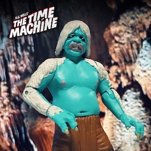 Op de afbeelding: Een blauwe en witte action figure van een wezen uit de film "The Time Machine" van H.G. Wells. De figuur heeft lang wit haar en een bruine lendendoek.