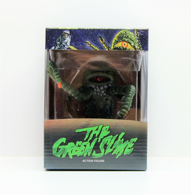 Op de afbeelding: Een groene en zwarte action figure van The Green Slime uit de film van 1968. De figuur zit in een doorzichtige plastic doos met een zwarte en groene achtergrond. De doos heeft de tekst "The Green Slime" en "Action Figure" erop.