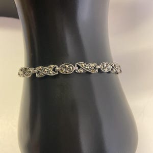Puede incluir: Un brazalete de plata con un delicado diseño de cadena adornado con pequeñas piedras de marcasita negras.
