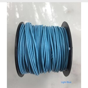 Könnte beinhalten: Eine Spule hellblaues Lederband. Das Band ist eng um eine schwarze Kunststoffspule gewickelt. Der Text "Light Blue" ist auf dem Bild zu sehen. Dieses Lederband ist 1,5 mm dick.