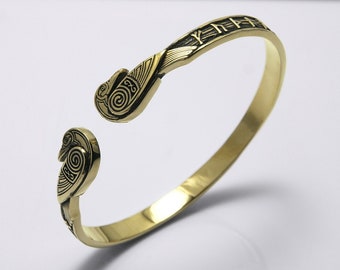 May include: A gold-toned bangle bracelet with intricate Celtic knot designs on the ends. The bracelet is open and has a simple, polished finish.