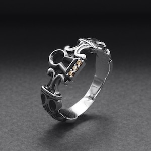 May include: A silver ring with an intricate design and small clear stones.