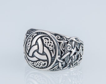 May include: A silver ring with a Celtic knot design. The ring features a central motif of a triskelion, a symbol of three interlocked spirals, surrounded by intricate knotwork.