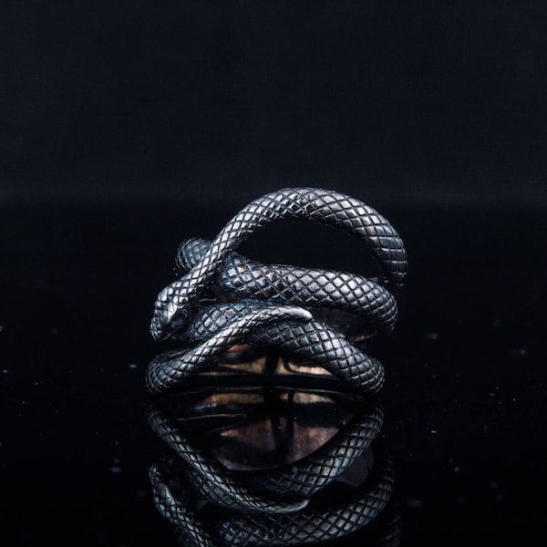 May include: A silver ring with a detailed snake design. The snake is coiled around itself, with its head and tail visible. The ring is made of metal and has a polished finish.