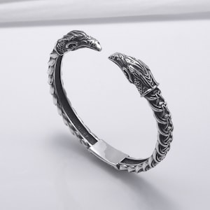 May include: Silver bracelet with a detailed design of two dragon heads on the ends.