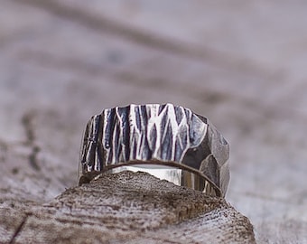 May include: A silver ring with a textured, hammered finish. The ring is wide and has a rounded shape.