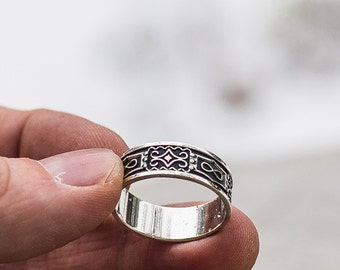 May include: A silver ring with an intricate design. The ring is worn on a finger.