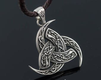 Puede incluir: Colgante plateado con diseño de triquetra, con intrincados nudos y cuernos curvados. El colgante cuelga de un cordón marrón oscuro. La imagen incluye el texto "UNIQUE HISTORY SHOP".
