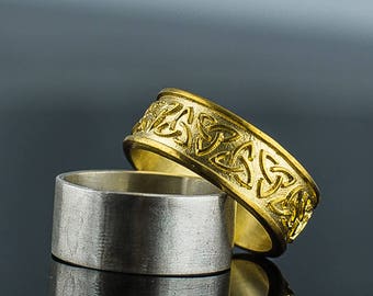 May include: Two wedding bands, one gold and one silver. The gold band has a Celtic knot design.