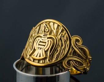 May include: A gold ring with a detailed design of a bird with its wings spread. The ring is set on a silver band. The ring is a unique piece of jewelry that would make a great gift for anyone who loves birds or Norse mythology.