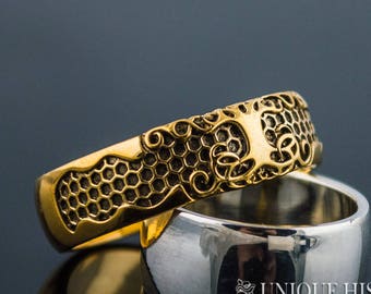 May include: A gold ring with a tree of life design and a honeycomb pattern. The ring is on top of a silver ring.