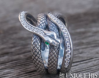 May include: A silver ring with a coiled snake design, featuring a green gemstone eye and clear cubic zirconia stones.