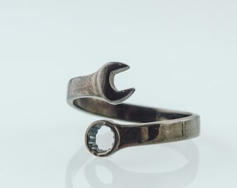 May include: A silver adjustable ring shaped like a wrench with a clear crystal in the center.