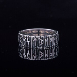 Op de afbeelding: Een zilveren ring met een getextureerde band en een patroon van Noorse runen rond de hele band.