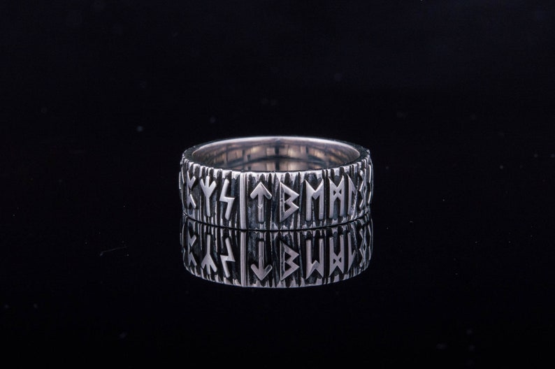 Op de afbeelding: Een zilveren ring met een getextureerde band en een patroon van Noorse runen rond de hele band.