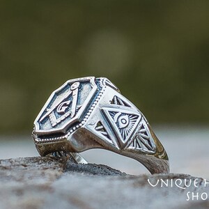 K&ouml;nnte beinhalten: Ein silberner Ring mit einem freimaurerischen Symbol und einem All-Seeing-Eye-Design. Der Ring ist aus Sterlingsilber gefertigt und hat eine polierte Oberfl&auml;che.