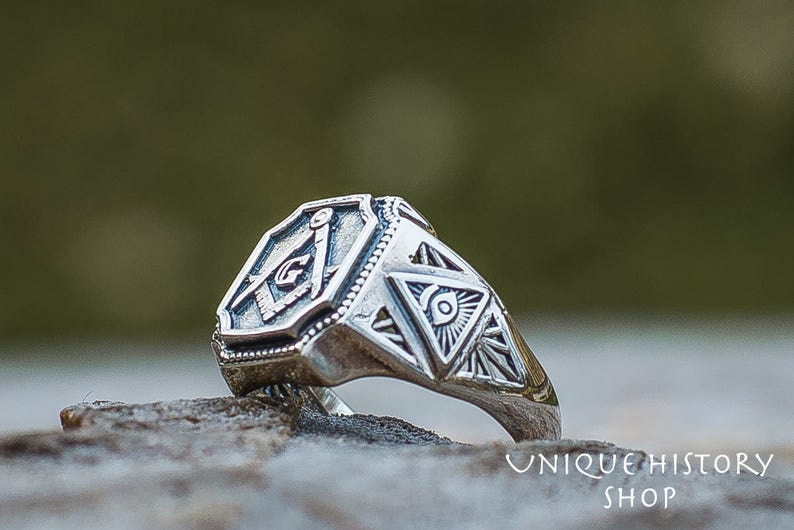 K&ouml;nnte beinhalten: Ein silberner Ring mit einem freimaurerischen Symbol und einem All-Seeing-Eye-Design. Der Ring ist aus Sterlingsilber gefertigt und hat eine polierte Oberfl&auml;che.