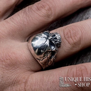 Pu&ograve; includere: Un anello d'argento a forma di teschio con dettagli elaborati. L'anello &egrave; indossato su un dito.