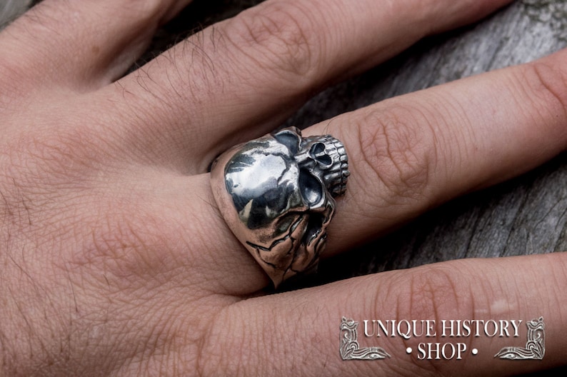 Pu&ograve; includere: Un anello d'argento a forma di teschio con dettagli elaborati. L'anello &egrave; indossato su un dito.