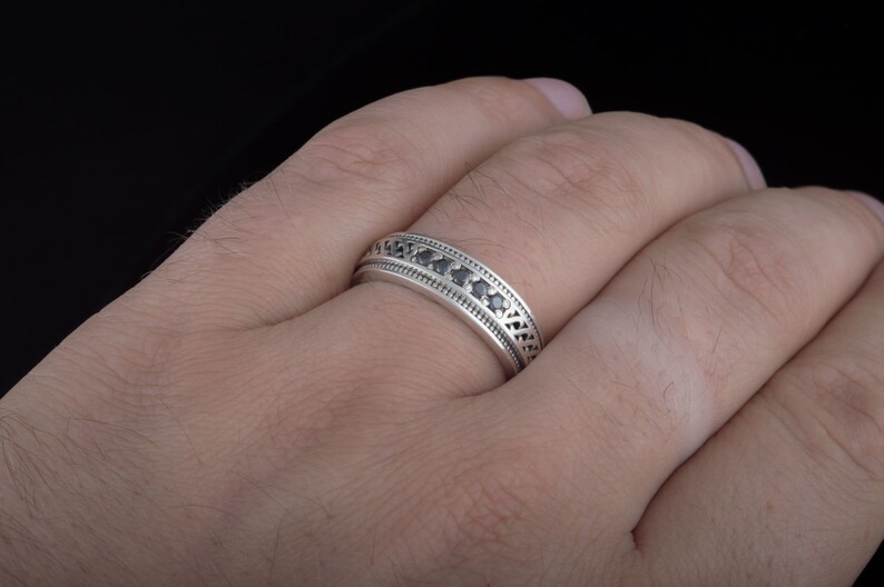 May include: A silver band ring with a row of black gemstones set in a decorative pattern.