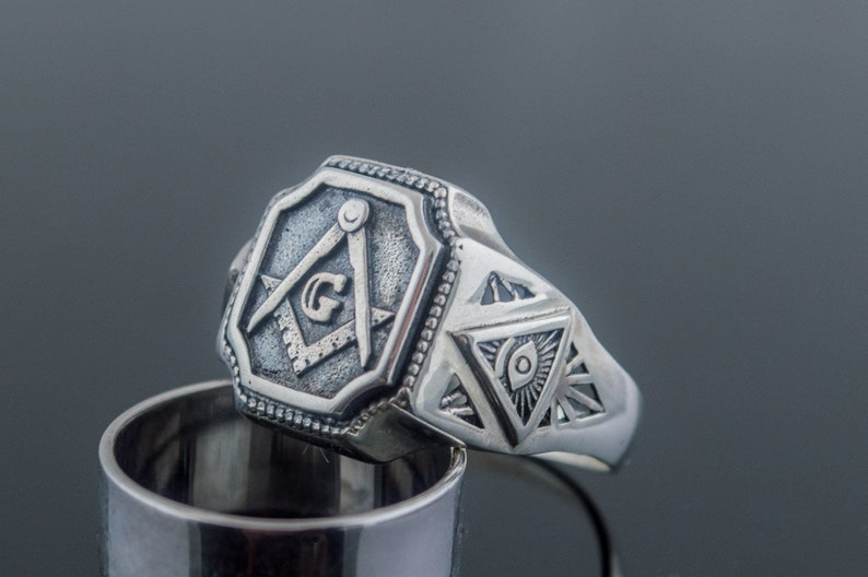 K&ouml;nnte beinhalten: Silberner Freimaurer-Ring mit einem Quadrat- und Zirkel-Design und einem allsehenden Auge in einem Dreieck.