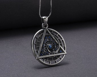 Puede incluir: Collar con colgante de plata con un diseño circular que presenta un triángulo con un ojo en el centro. El ojo está rodeado de pequeñas piedras preciosas azules.
