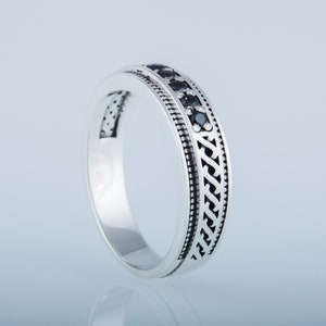 May include: A silver band ring with a black stone inlay and a decorative pattern.