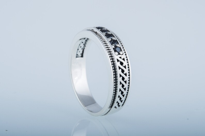 May include: A silver band ring with a black stone inlay and a decorative pattern.